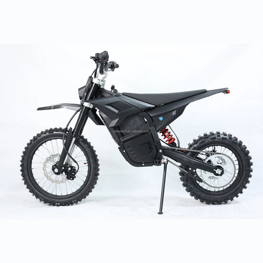 A black electric dirt bike with knobby tires, a black seat, and a visible red rear shock absorber, photographed on a white studio background with the kickstand down.