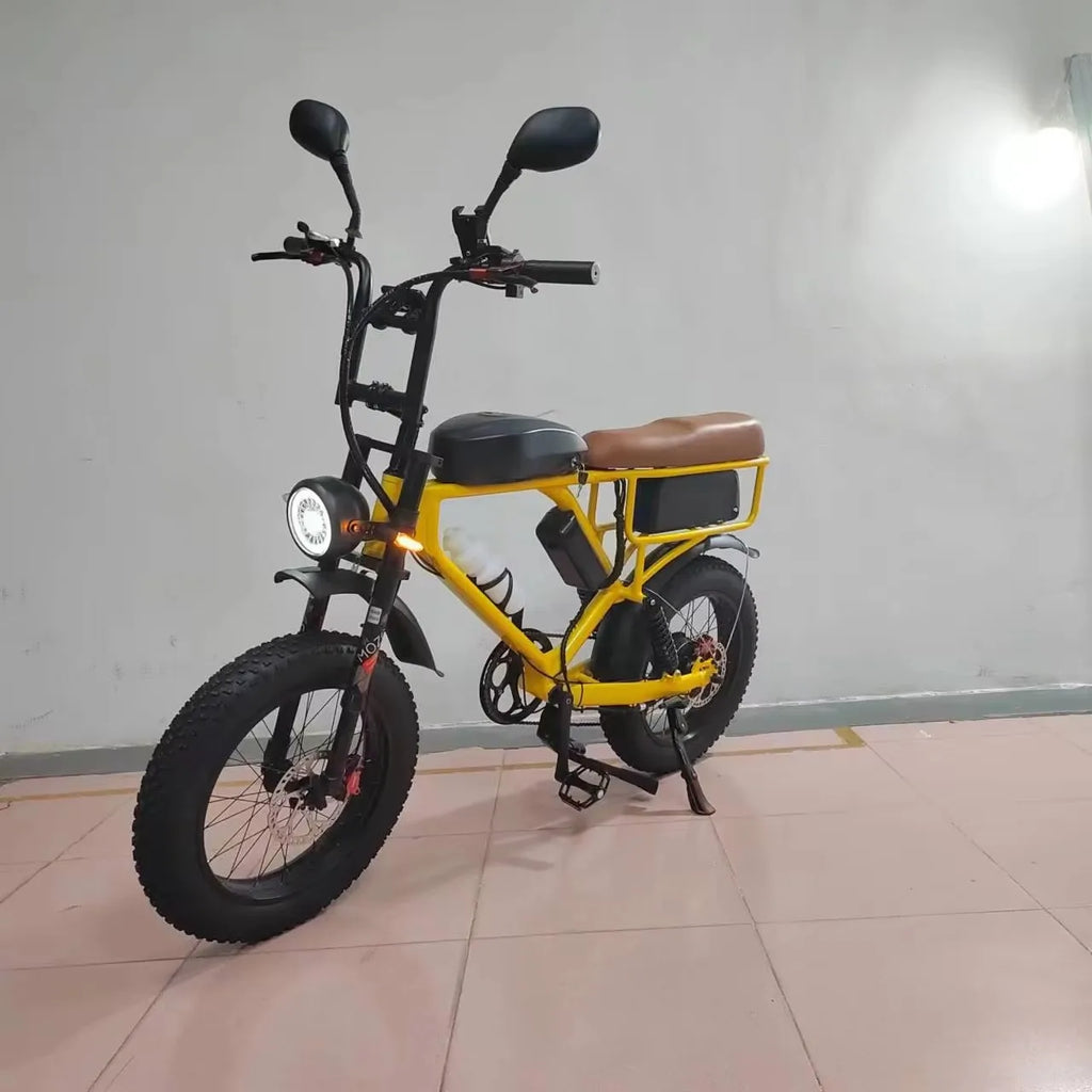 A yellow and black mini electric bicycle with fat tires, a brown saddle, and rear cargo rack, shown on a tiled floor against a plain wall.