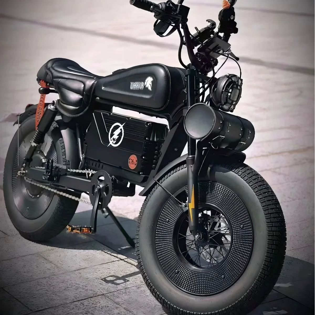 A black custom electric motorcycle with fat tires, a low seat, and a fuel tank, photographed on a paved outdoor surface.