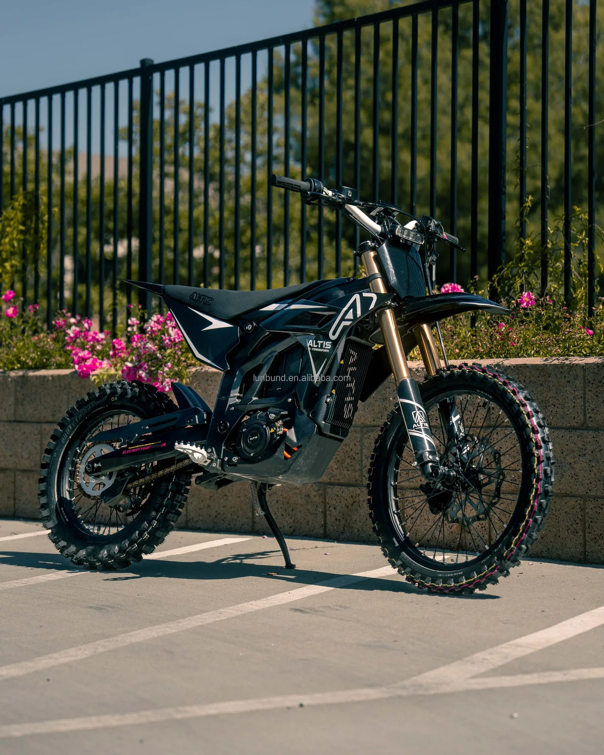 Motorcycle parked on a concrete surface with a metal fence and flowers in the background