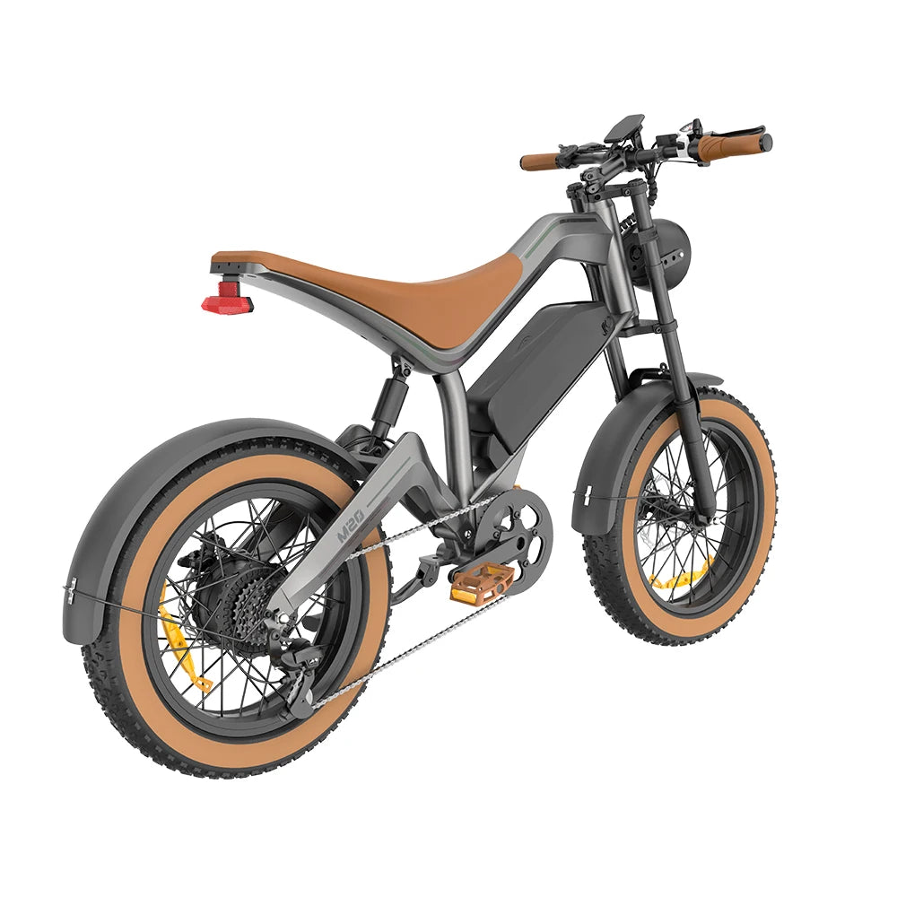 A modern electric fat-tire bicycle with a matte gray frame, brown leather saddle, and tan sidewall tires, shown from a three-quarters rear angle on a white background.