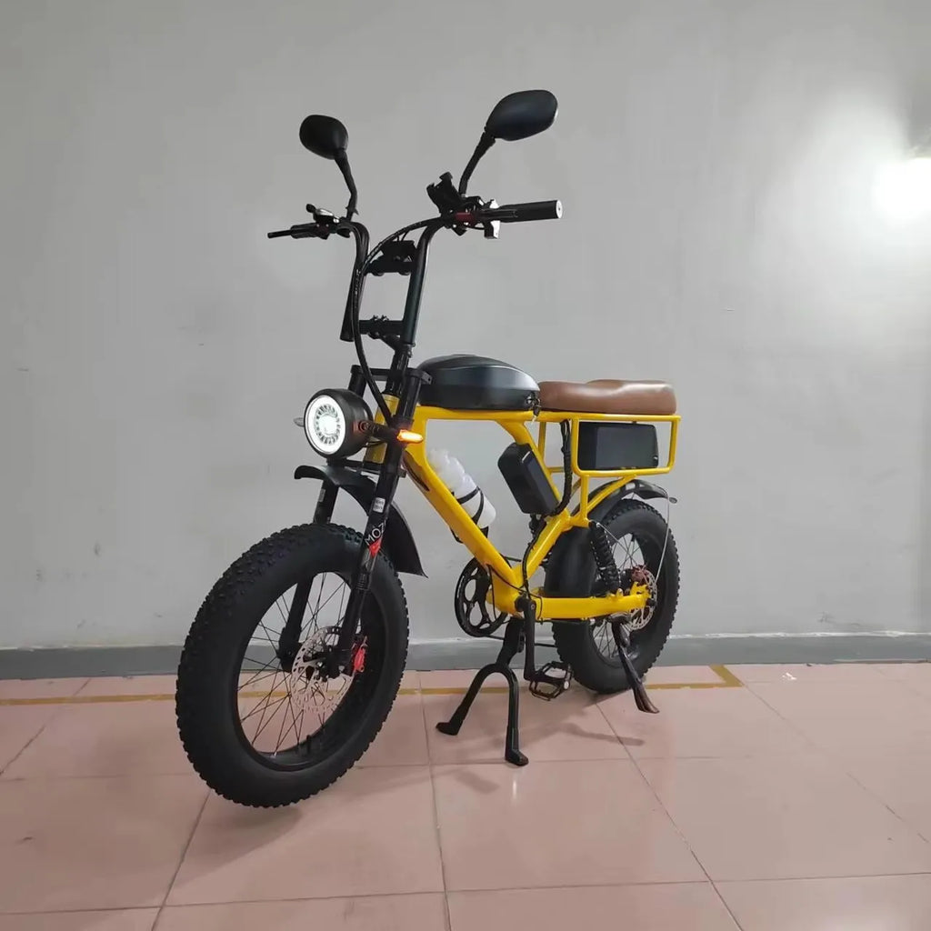 A yellow and black mini electric fat-tire bike with a brown saddle, front headlight, and rear storage box, shown on a kickstand in an indoor setting.