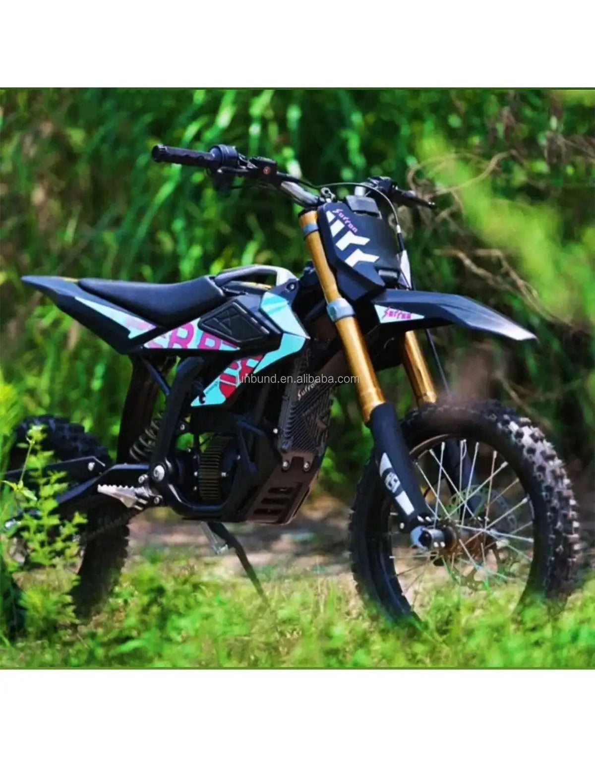 A black electric dirt bike with gold front forks and pink and blue graphics, parked outdoors on grass with a blurred green forest background.