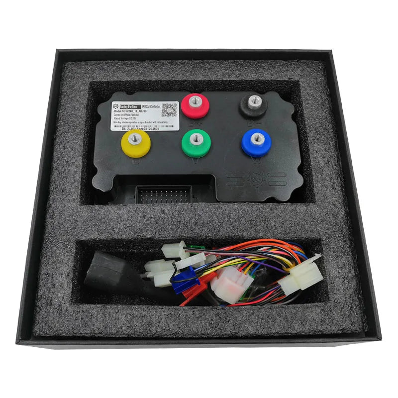 An electronic control module kit with four colored buttons (red, green, blue, yellow), a connector block, and a bundle of multi-colored wiring harnesses, presented in a black foam-lined box.