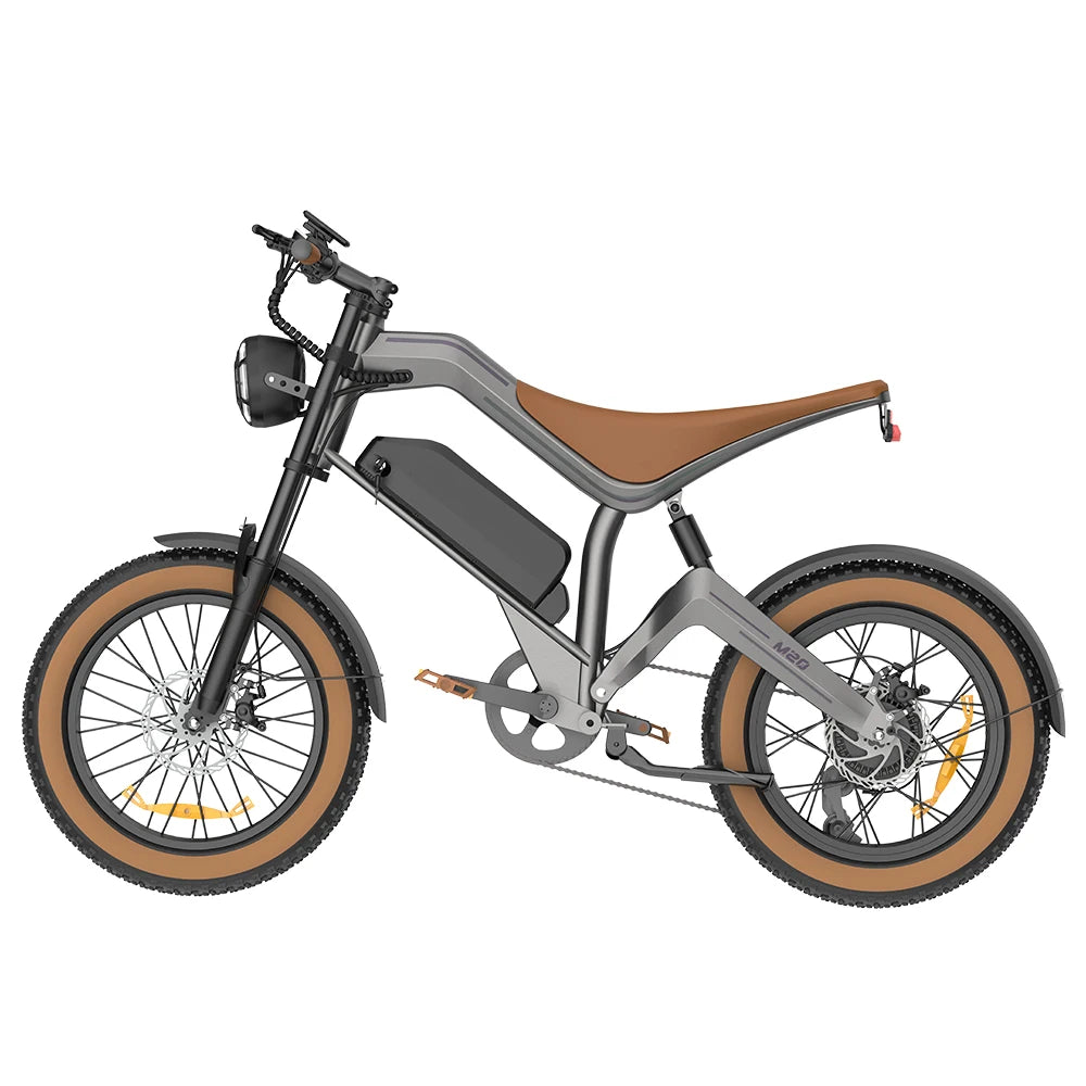 A modern electric fat-tire bicycle with a matte gray frame, a brown saddle, and tan sidewall tires, shown from a side profile on a solid white background.