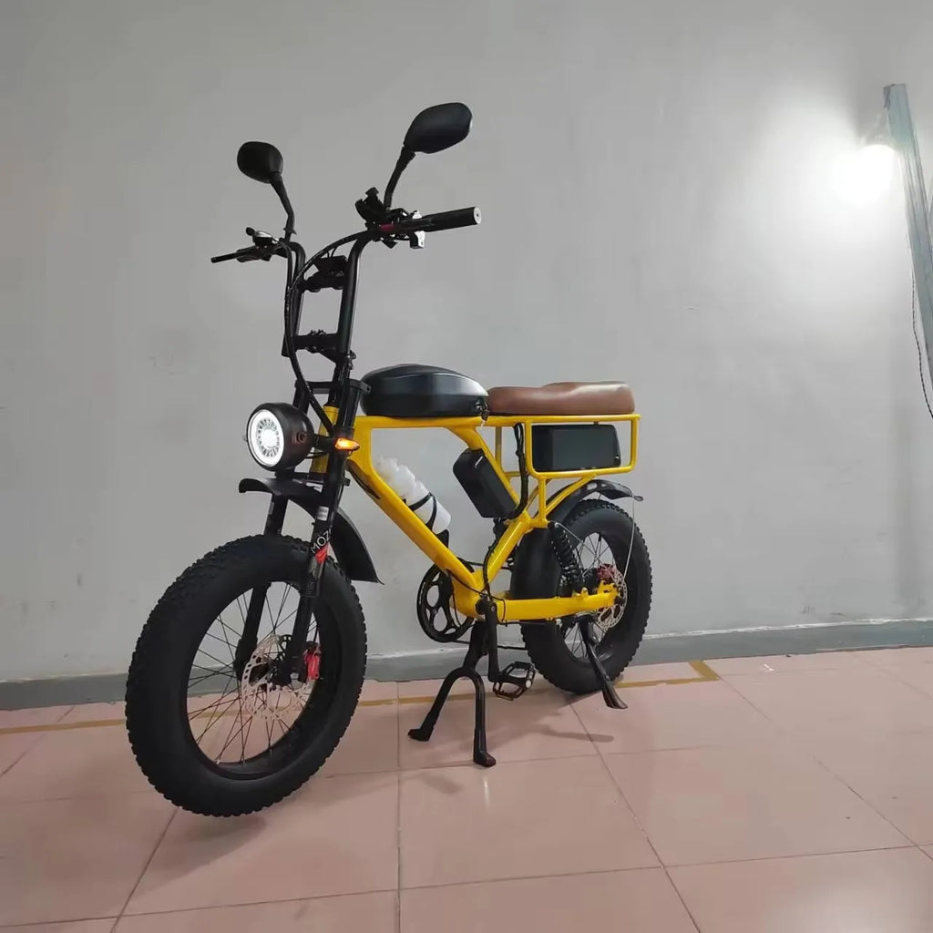 A yellow and black electric fat-tire bicycle with a brown saddle, photographed indoors against a plain light gray wall on a tiled floor.