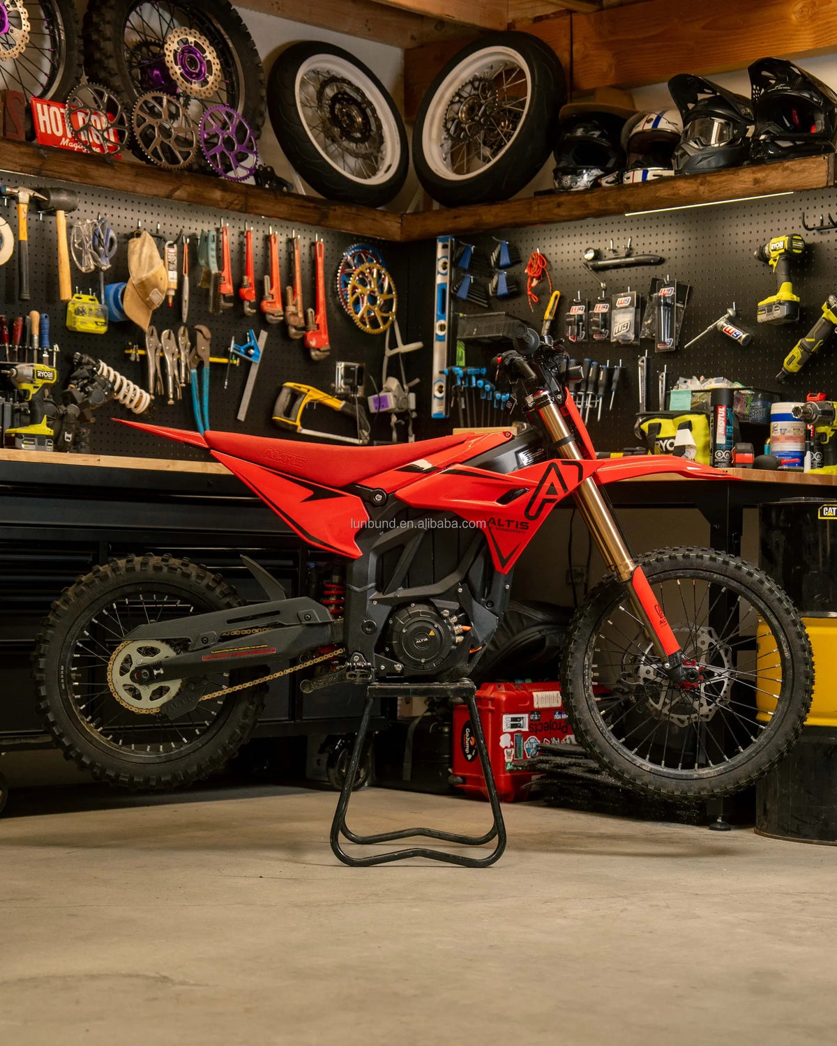 Red dirt bike on a stand in a workshop with tools and tires in the background