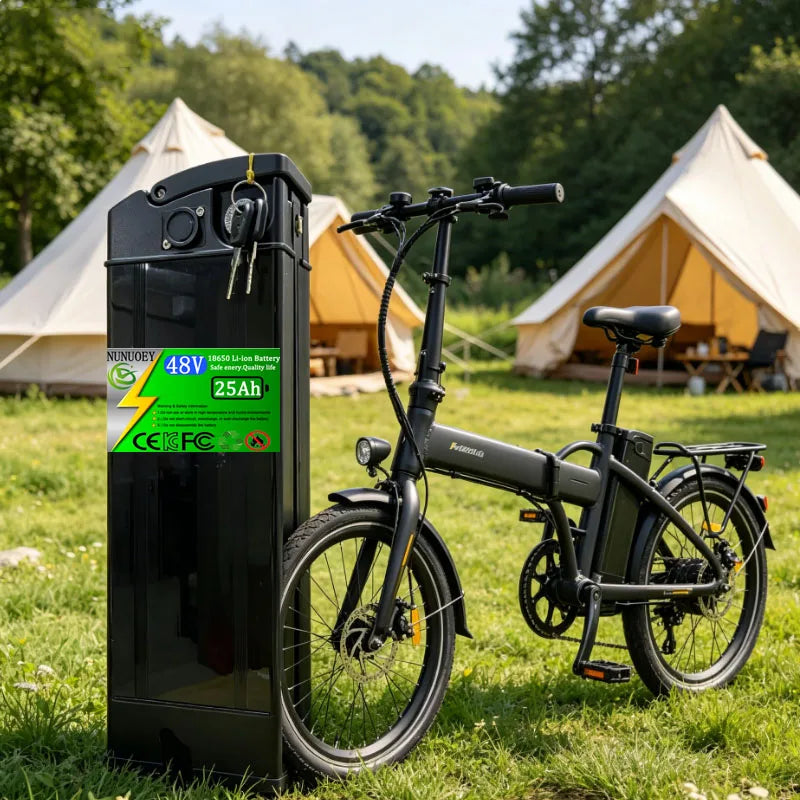 A folding electric bicycle in matte black is parked outdoors on grass next to a tall black battery charger or storage unit with a bright green label. Three canvas tents are visible in the background among trees.