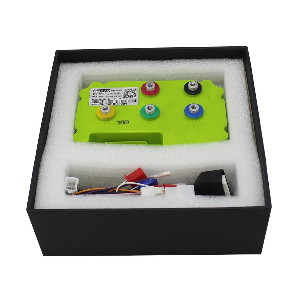 A green electronic control module with four colored terminal buttons and attached wiring, presented in a black box with white foam insert.