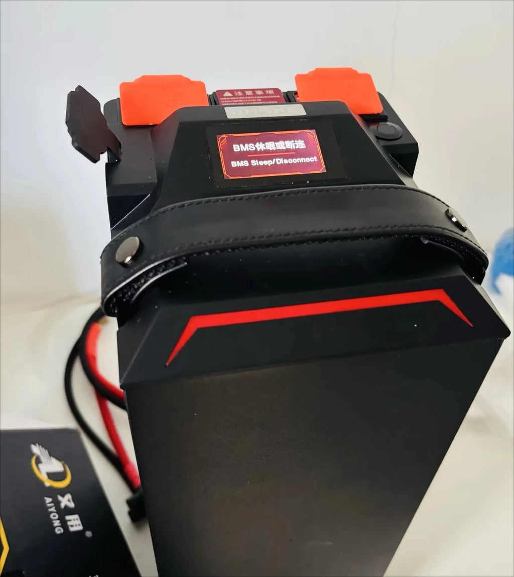 A black BMS (Battery Management System) snap disconnect battery with orange terminal covers and a red label, shown with its attached red and black cable on a light background.