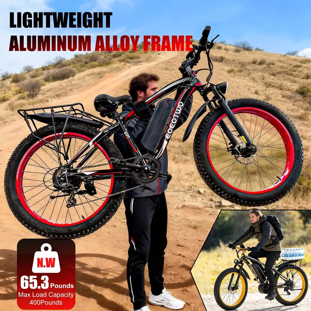 Person carrying a black electric bike with red rims on a dirt path.