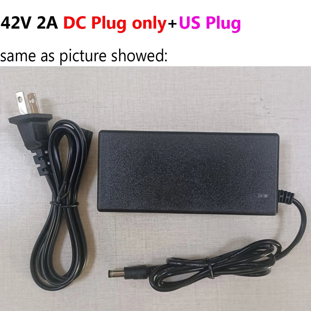 Black 42V 2A DC power adapter with a US plug, shown alongside a standard US wall outlet on a light gray textured background. Text at the top reads '42V 2A DC Plug only+US Plug' and 'same as picture showed:'.