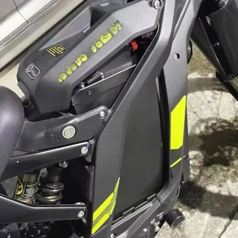 Close-up of a black scooter or motorcycle body panel with bright yellow-green graphic accents and stylized lettering, photographed outdoors on a concrete surface.