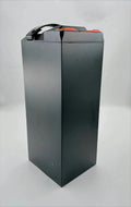 A tall rectangular black battery with a top handle and small orange terminal caps, photographed on a plain light gray studio background.