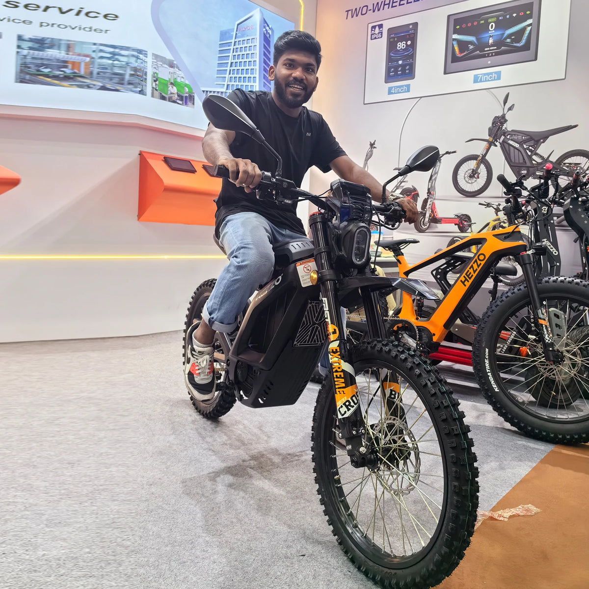 Man sitting on an electric bike in a showroom with multiple bikes and digital displays in the background.