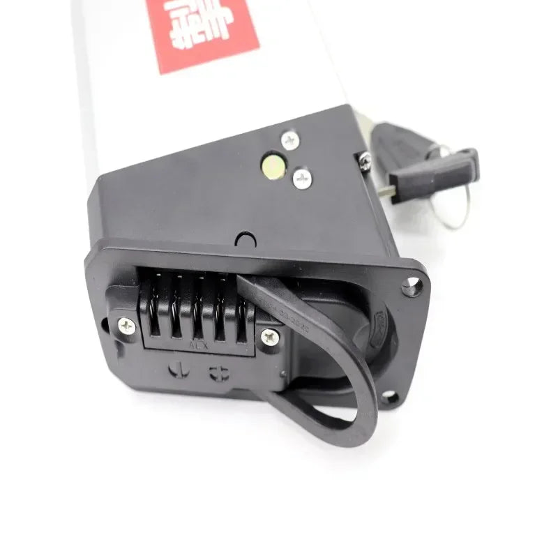 A close-up of a black plastic mechanical component or bracket with a latch-like tab, shown on a white background with part of a white rectangular item and a red label visible behind it.